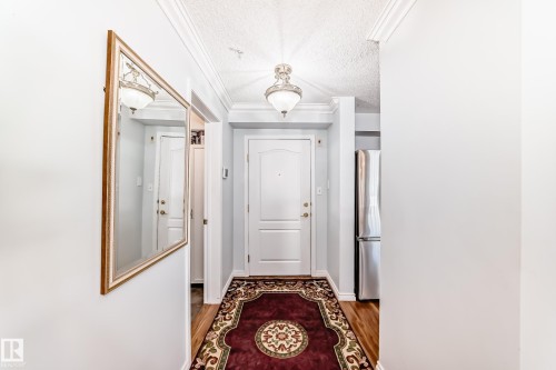 Entryway featuring wood floors, crown molding, a decorative ceiling light fixture, and a white paneled door - 112 17150 94A Avenue, Edmonton, AB - Indoor Photo Showing Other Room