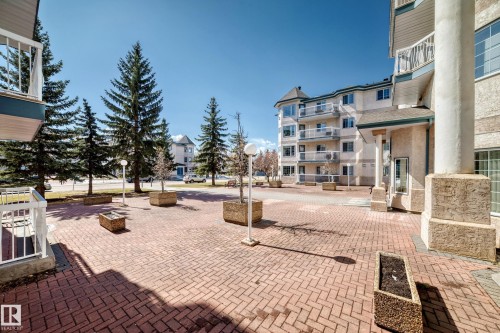 Exterior view of the property featuring a brick paved courtyard with planter boxes and mature trees - 112 17150 94A Avenue, Edmonton, AB - Outdoor