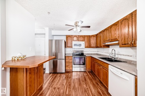 The kitchen features wood cabinetry, a stainless steel refrigerator, and a built-in oven with a microwave above - 112 17150 94A Avenue, Edmonton, AB - Indoor Photo Showing Kitchen With Double Sink