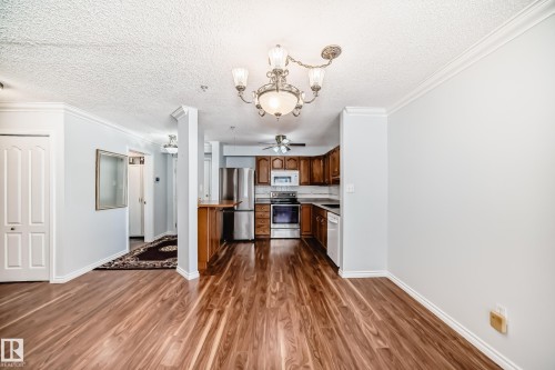 This open concept living area features wood flooring, light-colored walls, and a view of the kitchen - 112 17150 94A Avenue, Edmonton, AB - Indoor Photo Showing Kitchen