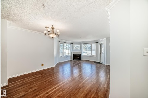 The property features rich hardwood floors, a classic chandelier, a corner fireplace, and numerous windows - 112 17150 94A Avenue, Edmonton, AB - Indoor With Fireplace