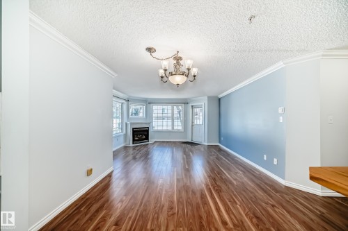 Inviting living space featuring hardwood floors, a fireplace with a white mantel, and a bay window providing natural light - 112 17150 94A Avenue, Edmonton, AB - Indoor Photo Showing Other Room With Fireplace