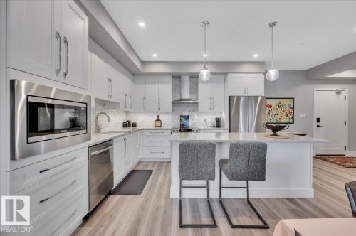 STAINLESS STEEL APPLIANCES AND PENDANT LIGHTING OVER THE LARGE ISLAND - 404 7463 May Common Nw, Edmonton, AB - Indoor Photo Showing Kitchen With Stainless Steel Kitchen With Upgraded Kitchen