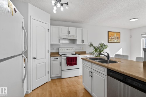 The kitchen features white cabinetry, light wood-toned countertops, a stainless steel dishwasher, and a double basin sink with a modern faucet - 421 84 Street, Edmonton, AB - Indoor Photo Showing Kitchen With Double Sink