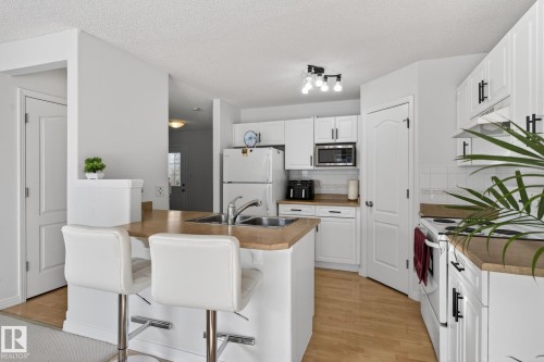 The kitchen features white cabinetry, wood-look countertops, and stainless steel appliances - 421 84 Street, Edmonton, AB - Indoor Photo Showing Kitchen With Double Sink