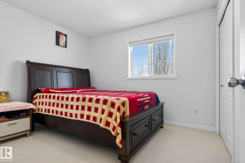 This room features light-colored walls and carpeting, a window with a view of trees, and a closet with bifold doors - 421 84 Street, Edmonton, AB - Indoor Photo Showing Bedroom