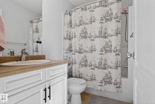 This bathroom features a vanity with a counter and an integrated sink, a mirror, and a toilet - 421 84 Street, Edmonton, AB - Indoor Photo Showing Bathroom