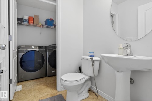Convenient laundry area featuring a washer and dryer, with an adjacent bathroom featuring a toilet, pedestal sink, and a circular wall mirror - 421 84 Street, Edmonton, AB - Indoor Photo Showing Laundry Room