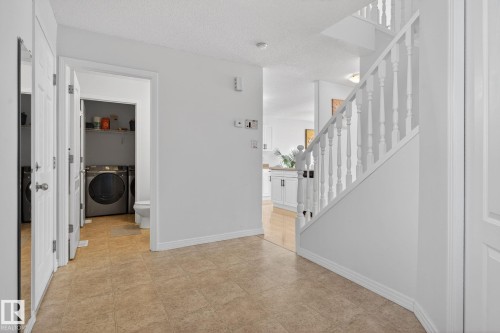 The property features a staircase with white balusters, tiled flooring in the entryway, and a laundry area with a washer and dryer - 421 84 Street, Edmonton, AB - Indoor Photo Showing Other Room