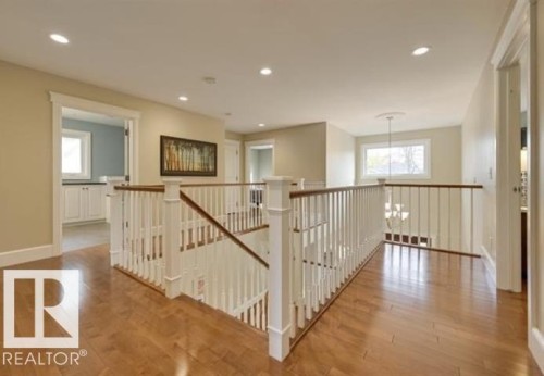 This bright hallway features rich hardwood floors, a white banister with a wood handrail, and recessed lighting - 10836 130 Street, Edmonton, AB - Indoor Photo Showing Other Room