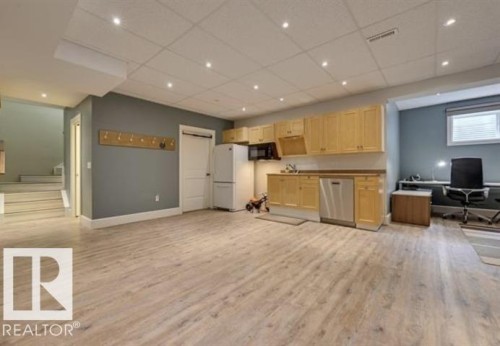 Expansive room with light-toned flooring, recessed lighting, and a partial kitchen featuring light wood cabinetry, a stainless steel dishwasher, and a white refrigerator - 10836 130 Street, Edmonton, AB - Indoor