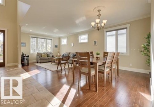 The property features an open-concept living area with rich hardwood flooring, large windows providing natural light, and a dining area illuminated by a classic chandelier - 10836 130 Street, Edmonton, AB - Indoor Photo Showing Dining Room