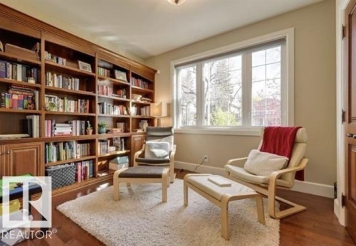 This inviting space features extensive built-in wooden shelving, large windows providing natural light, and hardwood floors - 10836 130 Street, Edmonton, AB - Indoor Photo Showing Office