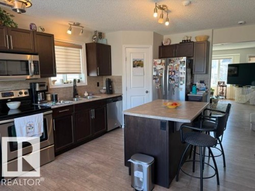 Well-appointed kitchen featuring dark wood cabinetry, stainless steel appliances, a light-colored countertop, and an island with seating - 21316 95 Avenue, Edmonton, AB - Indoor Photo Showing Kitchen With Stainless Steel Kitchen With Double Sink