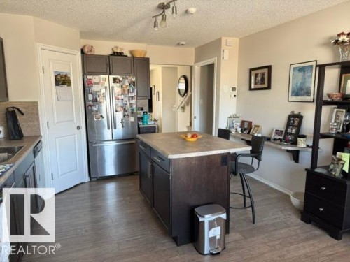 The kitchen features a central island with a countertop, dark cabinetry, and light-toned flooring - 21316 95 Avenue, Edmonton, AB - Indoor Photo Showing Kitchen