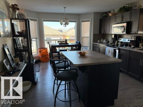 The kitchen features dark cabinetry, stainless steel appliances, and a central island with a light-colored countertop - 21316 95 Avenue, Edmonton, AB - Indoor Photo Showing Kitchen