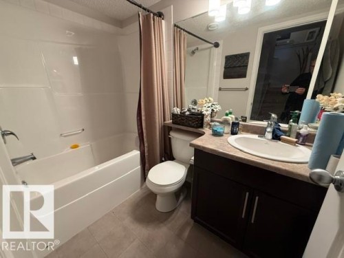 This bathroom features a white bathtub with a shower, a dark wood vanity with a light-colored countertop, and a large mirror with overhead lighting - 21316 95 Avenue, Edmonton, AB - Indoor Photo Showing Bathroom