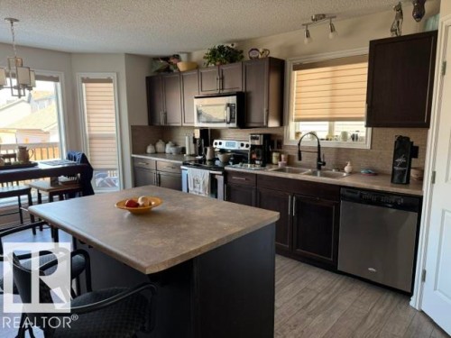 The kitchen features dark cabinetry, a central island, stainless steel appliances, and wood-look flooring - 21316 95 Avenue, Edmonton, AB - Indoor Photo Showing Kitchen With Double Sink