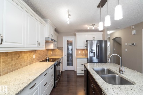 The kitchen features white cabinetry, granite countertops, and stainless steel appliances, including a double-door refrigerator and a range - 132 Kirpatrick Way, Leduc, AB - Indoor Photo Showing Kitchen With Double Sink With Upgraded Kitchen