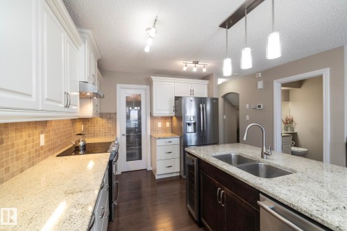Well-appointed kitchen featuring white cabinetry, light-toned granite countertops, a tiled backsplash, and stainless steel appliances - 132 Kirpatrick Way, Leduc, AB - Indoor Photo Showing Kitchen With Double Sink With Upgraded Kitchen