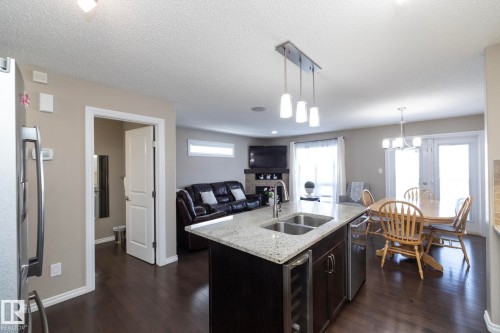 The property features an open concept kitchen and living area, complete with dark wood flooring - 132 Kirpatrick Way, Leduc, AB - Indoor Photo Showing Kitchen With Double Sink