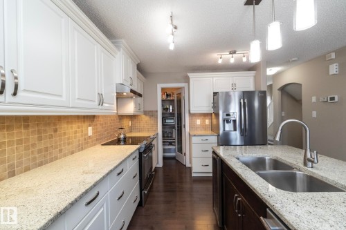 The kitchen features white cabinetry, granite countertops, a tiled backsplash, and stainless steel appliances - 132 Kirpatrick Way, Leduc, AB - Indoor Photo Showing Kitchen With Double Sink With Upgraded Kitchen