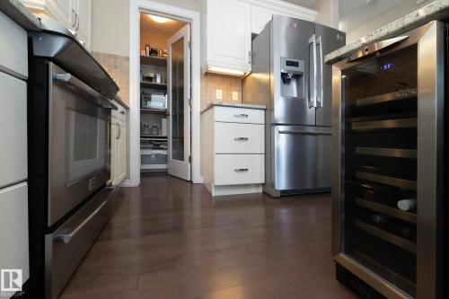 The property features a kitchen with white cabinetry, stainless steel appliances, granite countertops, and hardwood flooring - 132 Kirpatrick Way, Leduc, AB - Indoor Photo Showing Kitchen