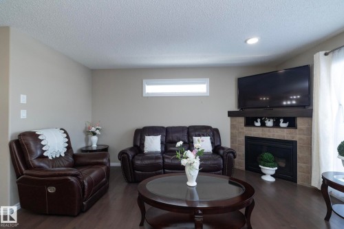 Living area featuring dark hardwood floors, a corner fireplace with tile surround and a dark wood mantel, and a horizontal window - 132 Kirpatrick Way, Leduc, AB - Indoor Photo Showing Living Room With Fireplace
