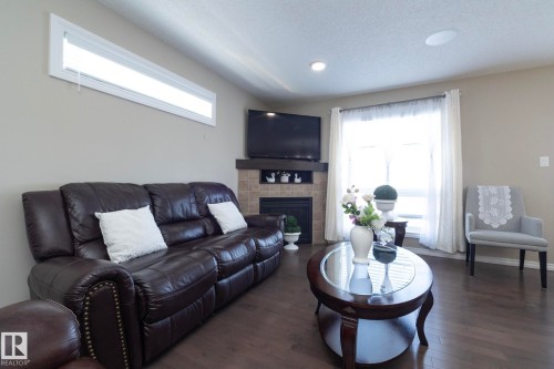 The living area features hardwood style flooring, a tiled fireplace with a mantel, and recessed lighting - 132 Kirpatrick Way, Leduc, AB - Indoor With Fireplace