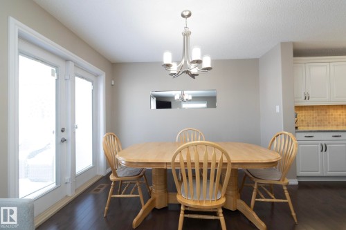 Dining area featuring a contemporary chandelier, hardwood floors, and a pair of glass panel doors - 132 Kirpatrick Way, Leduc, AB - Indoor Photo Showing Dining Room