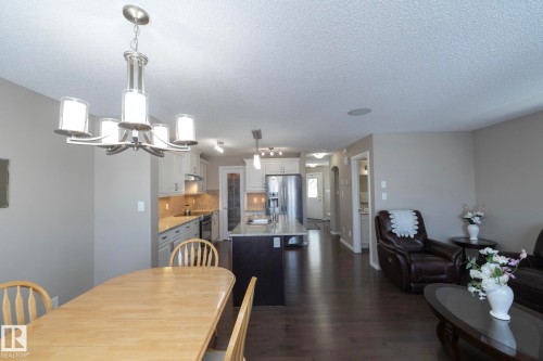 Open concept living area with hardwood floors, a kitchen featuring white cabinetry and stainless steel appliances, and a dining area with a chandelier - 132 Kirpatrick Way, Leduc, AB - Indoor Photo Showing Dining Room