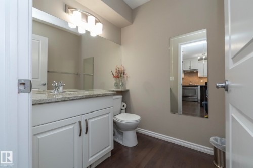 This bathroom features a white vanity with granite countertops, a large mirror, a toilet, and dark wood flooring - 132 Kirpatrick Way, Leduc, AB - Indoor Photo Showing Bathroom