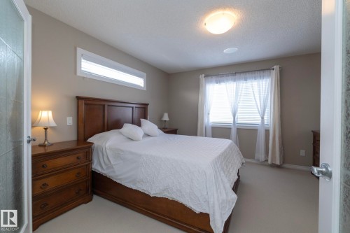 This bedroom features a high window with blinds, a window with blinds and sheer curtains, and light-colored carpet - 132 Kirpatrick Way, Leduc, AB - Indoor Photo Showing Bedroom