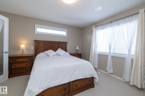 This bedroom features a light neutral color palette, wood furnishings, and a large window with privacy blinds and sheer curtains - 132 Kirpatrick Way, Leduc, AB - Indoor Photo Showing Bedroom
