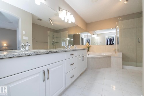 Bathroom featuring a double vanity with white cabinetry and a light-colored countertop, a built-in bathtub, a glass-enclosed shower, and light-colored tile flooring - 132 Kirpatrick Way, Leduc, AB - Indoor Photo Showing Bathroom
