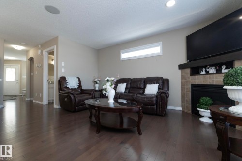This inviting living area features dark wood flooring, a fireplace with a tiled surround and mantel, and a window providing natural light - 132 Kirpatrick Way, Leduc, AB - Indoor Photo Showing Living Room With Fireplace