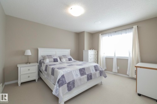 This room features light-colored walls and carpeting, a window with sheer white curtains, and a ceiling light fixture - 132 Kirpatrick Way, Leduc, AB - Indoor Photo Showing Bedroom