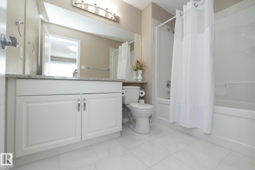 Bathroom featuring a white vanity with a granite countertop, a toilet, a bathtub with a shower, and light-colored floor tiles - 132 Kirpatrick Way, Leduc, AB - Indoor Photo Showing Bathroom