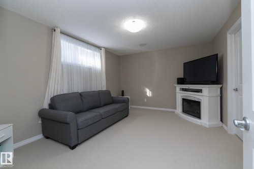 This room features neutral-toned walls, light-colored carpeting, a window with sheer and opaque curtains, and a corner-fitted white mantelpiece - 132 Kirpatrick Way, Leduc, AB - Indoor Photo Showing Living Room