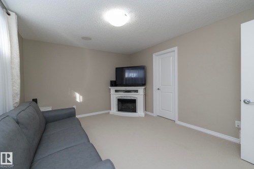 This living space features light-colored walls, carpeted flooring, and a corner fireplace - 132 Kirpatrick Way, Leduc, AB - Indoor