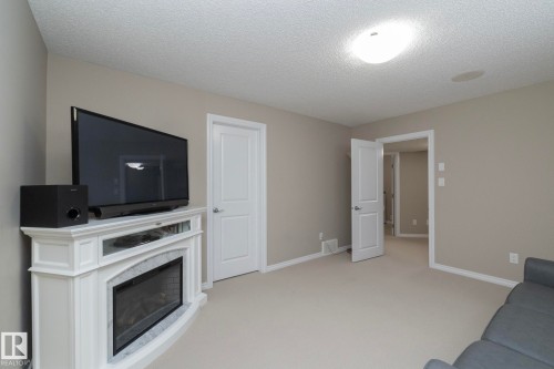 This room features light-colored walls, a ceiling light fixture, and a built-in electric fireplace with a white mantel and marble-look surround - 132 Kirpatrick Way, Leduc, AB - Indoor