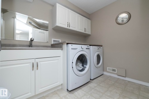 Laundry area featuring a sink with a faucet, white cabinetry, and a washer and dryer - 132 Kirpatrick Way, Leduc, AB - Indoor Photo Showing Laundry Room