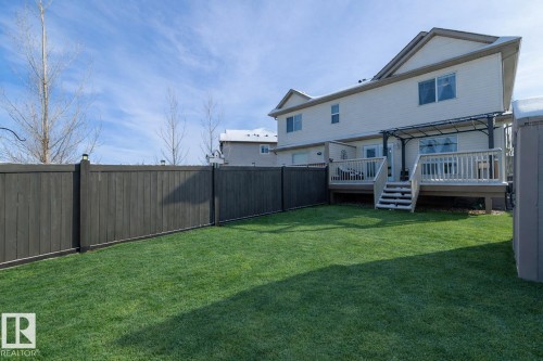 The property features a spacious backyard with a well-maintained lawn and a private wooden fence - 132 Kirpatrick Way, Leduc, AB - Outdoor With Deck Patio Veranda