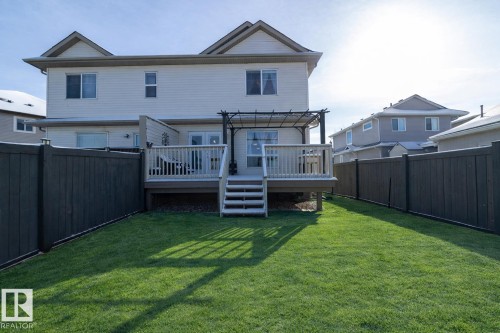 The property includes a spacious backyard with a well-maintained lawn, a wooden deck with railing, and privacy fencing - 132 Kirpatrick Way, Leduc, AB - Outdoor With Deck Patio Veranda