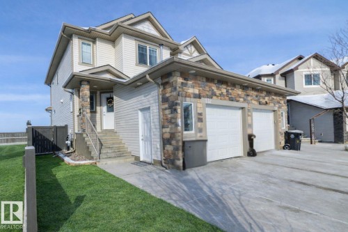 The property features a two-car garage with white doors, a stone facade, and a well-maintained lawn - 132 Kirpatrick Way, Leduc, AB - Outdoor