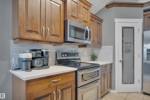 The kitchen features rich wood cabinetry, a stainless steel microwave and stove, light-colored countertops, and a tiled backsplash - 316 Avena Link, Leduc, AB - Indoor Photo Showing Kitchen