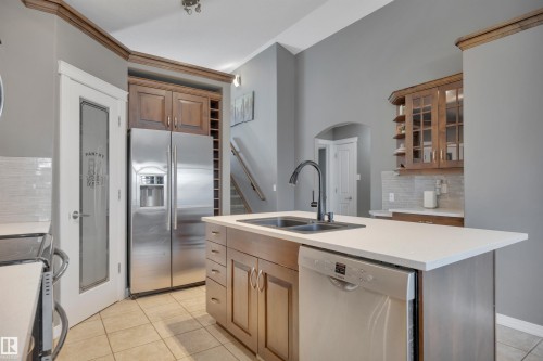 The kitchen features a central island with a double sink and a stainless steel dishwasher, along with a pantry door with frosted glass, and stainless steel refrigerator - 316 Avena Link, Leduc, AB - Indoor Photo Showing Kitchen With Double Sink
