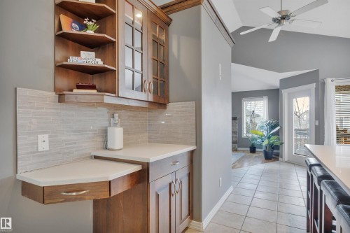 This property features a custom built-in cabinet with glass-front uppers and open corner shelving, a light-colored subway tile backsplash, and a counter space with a drawer - 316 Avena Link, Leduc, AB - Indoor