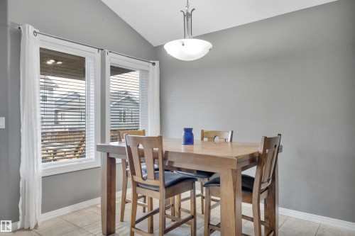Dining area featuring a vaulted ceiling with a hanging light fixture, two windows with blinds and curtains, and tile flooring - 316 Avena Link, Leduc, AB - Indoor Photo Showing Dining Room