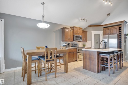 Kitchen featuring wood cabinetry, stainless steel appliances, a center island with seating, and tile flooring - 316 Avena Link, Leduc, AB - Indoor